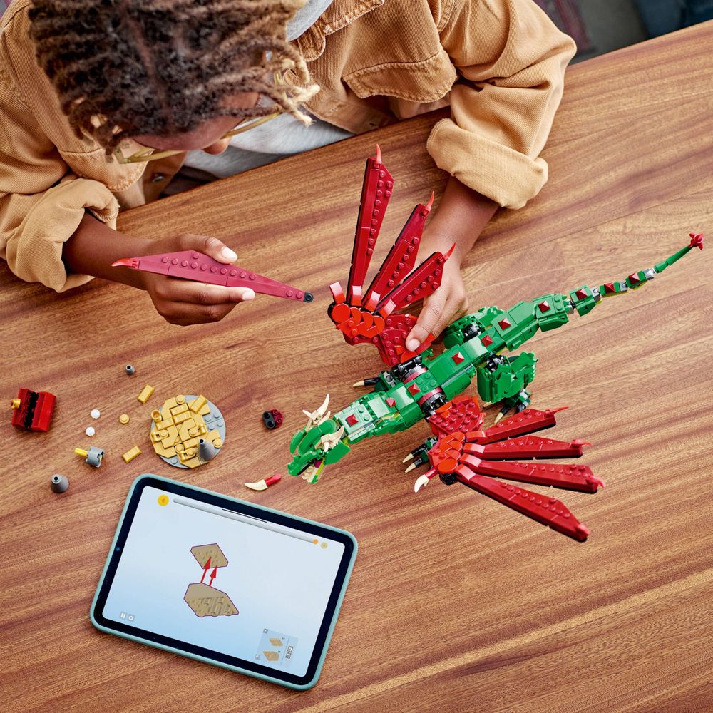 LEGO 31161 Ein Kind baut einen grünen Drachen mit roten Flügeln und nutzt ein Tablet für Anleitungen.