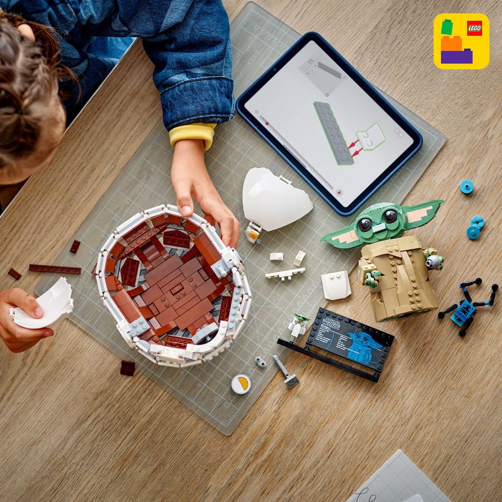 LEGO 75403 Ein Kind baut mit LEGO Steinen eine Repulsorwiege für Grogu mit Anleitung auf dem Tablet.