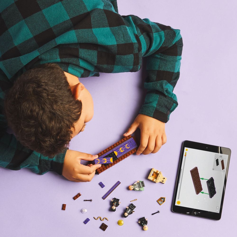 LEGO 76441 Ein Junge baut mit Lego umgeben von Bauteilen und einem Tablet für Anleitungen.