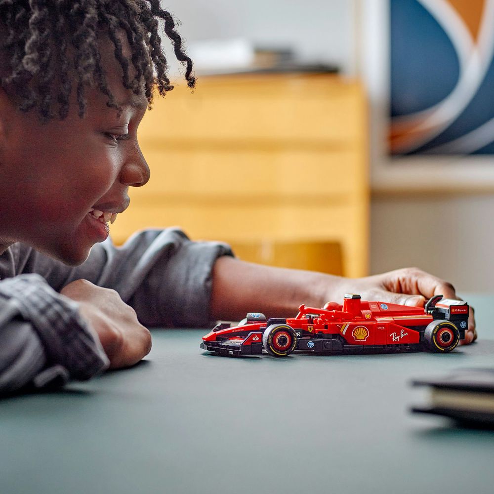 LEGO 77242 Ein Kind betrachtet ein rotes LEGO Formel 1 Auto auf einem Tisch begeistert und neugierig.